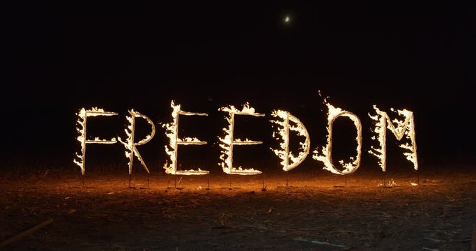 Cinematic shot of the Word FREEDOM Made of Bright, Glowing, Sparkling Pyrotechnic Fire Flames. Light Letters Burning During Festival or Carnival, Isolated Outdoors in the Dark at Night.
