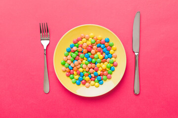 cutlery on table and sweet plate of candy. Health and obesity concept, top view on colored background