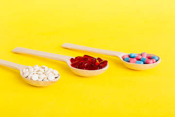 Vitamin capsules in a spoon on a colored background. Pills served as a healthy meal. Red soft gel vitamin supplement capsules on spoon