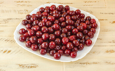 The fruits of ripe red cherry berries on a white square plate