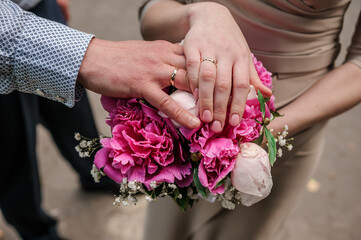 Obraz na płótnie Canvas Hands of newlyweds with wedding rings on a pink wedding bouquet of peonies
