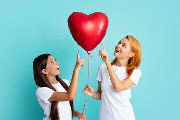 Fototapeta na wymiar Mothers day. Smiling mother and daughter isolated on blue background. Birthday holiday party, people emotions concept. Celebrating holding heard air balloons.