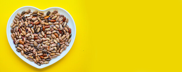 Banner. Dry beans on a white plate in the shape of a heart. Beans in a bowl isolated on a yellow background