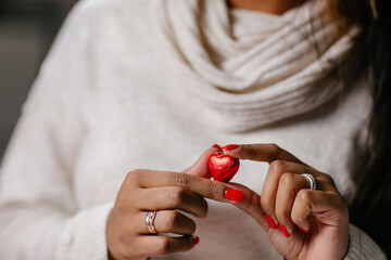 Women's hands with a bright manicure hold a heart-shaped chocolate candy