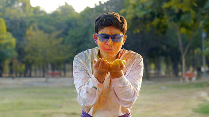 Cute Indian boy enjoying and playing with powder colors during Holi celebrations. A young cheerful...