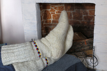 Warm knitted socks are worn on the feet. A man warms his feet near the fireplace.