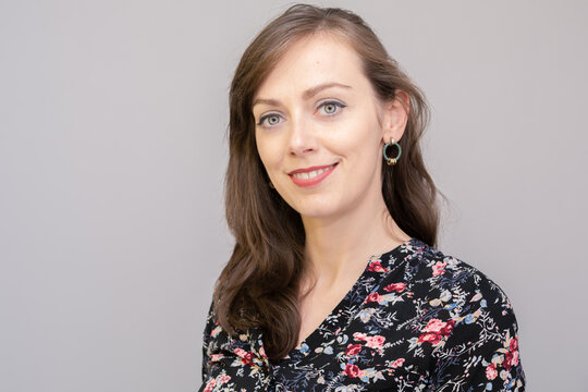 Beautiful young woman with big colorful eyes and natural smile. She is wearing dark floral blouse and green oval earrings. She is showing her white teets. Photo on plain grey background