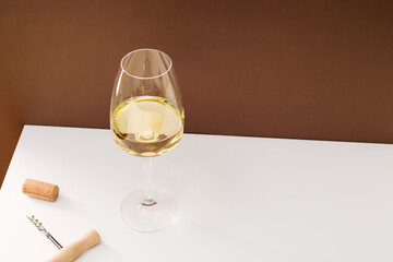 White wine in a glass, cork and bottle opener on a white table.