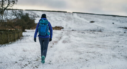 A hiker walking up a hill through the snow at Buckshott Fell in winter near Blanchland, Northumberland  in England UK.