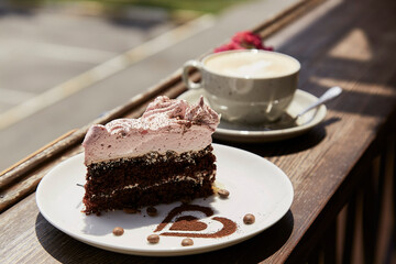 Aesthetic natural piece of cake and a glass of cappuccino on wooden table outdoor in the cafe terrace. Atmospheric breakfast. Hard shadows