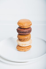 Stack of delicious freshly baked caramel, vanilla and chocolate flavoured macaron confections on white plate against white background. French sweet food speciality.