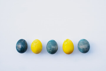 Natural dyed blue and yellow colored eggs on white background, top view, flat lay. Happy Easter. Copy space for text.