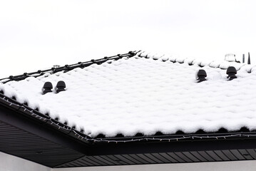 The roof of a single-family house is covered with snow against a cloudy sky, visible ceramic...