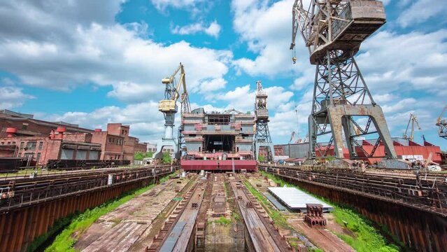 The construction of a large ship on a shipyard with cranes timelapse. A fragment of the case in the workshop of the plant. Metal frame during assembly front view. Cloudy sky