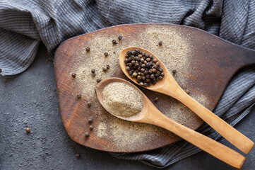 Heap of black pepper, peppercorns in spoon with milled powder on rustic background, dried spice...