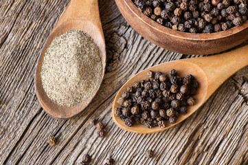 Heap of black pepper, peppercorns in spoon with milled powder on rustic background, dried spice peppercorn concept