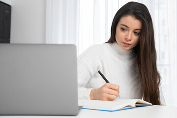 Serious young lady in stylish wear attends online lecture and makes notes with copy space. 
