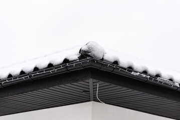 The roof of a single-family house is covered with snow against a cloudy sky, visible ridge tile on...