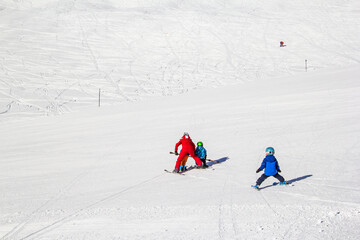 An adult is teaching kids with supporting ski poles to learn balance on snow piste