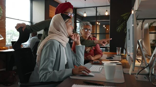 Team of creative business women having a discussion around a computer in a multicultural coworking office. Female professionals brainstorming ideas for a social media advertising campaign.