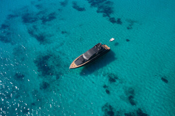 Dark blue yacht with teak wood in the morning sun top view. Large innovative modern yacht anchored on clear water aerial view.