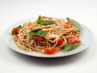 Close up of whole grain spaghetti pasta with cherry tomatoes, basil and parmesan cheese.