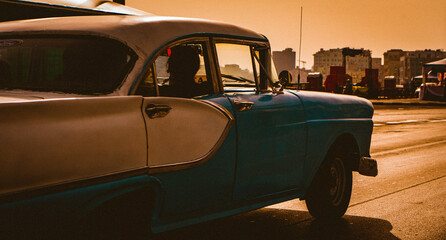legant classic Cuban car cruises the Malecon with a stylish passenger, as the sun sets on Havana, Cuba