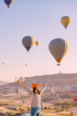 Happy traveller girl raising hands while watching magnificent view of flying hot air balloons in famous tourist attraction - Cappadocia © EdNurg