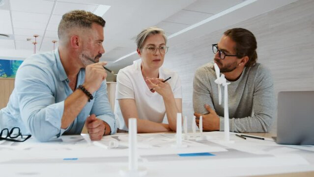 Three engineers discussing 3D models and drawings in a team meeting. Group of innovative business people collaborating on on a wind turbine design as part of a sustainable energy project.