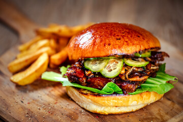 burger with pork ribs, served with cucumber and dipped teriyaki sauce on a wooden cutting board