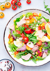 Tuna vegetables salad with cherry tomatoes, red onion, eggs, corn, paprika, lettuce, radicchio and arugula. Gray table background, top view