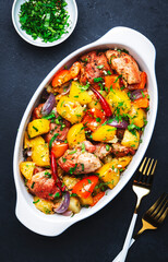 Baked turkey drumsticks fillet with potatoes, paprika, onions, herbs and spices in baking dish, black table background, top view