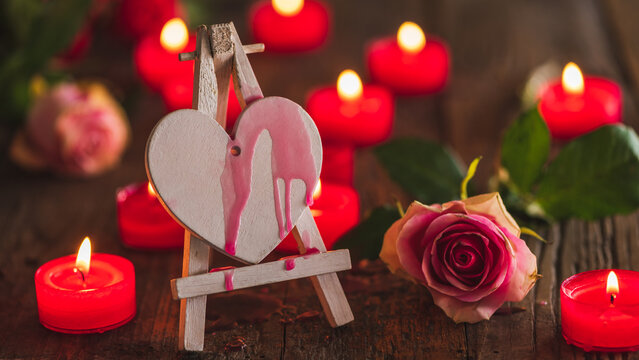 Valentines day or wedding concept, red wx running doen a white wooden heart on an easle, decorated with candle lughts and roses