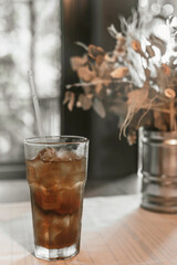 Beautiful still life with dried flowers in a tin vase and a long Island cocktail on the table by the window