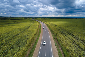 Fototapeta na wymiar Aerial view of intercity road between green agricultural fields with fast driving cars. Top view from drone of highway traffic
