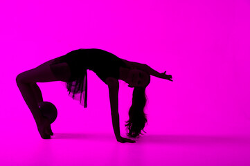 Silhouette of a gymnast who performs exercises with a ball. purple background
