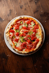 The top view of delicious Italian pizza with tomato cherry, ham, zucchini, mozzarella on the wooden background 