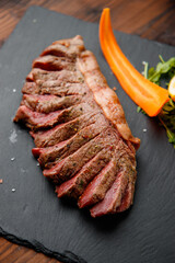 top view of delicious ribeye beef steak on the ribbon sliced on the black stone plate with carrots slices