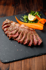 top view of delicious ribeye beef steak on the ribbon sliced on the black stone plate with carrots slices