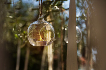 Pequeño candelabro esferérico colgante de vidrio con vela encendida, entre arboles decorados, Una imagen que brinda sensación pacifica, de fresca calma. 