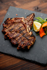 top view of delicious ribeye beef steak on the ribbon on the black stone plate with carrots slices