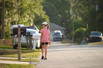 Rear view of confident young child girl walking along the sunny alley. Active lifestyle on summer holidays