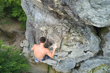 Strong male climber climbing steep wall of rocky mountain. Sportsman overcoming difficult route. Engaging in extreme sports hobby concept