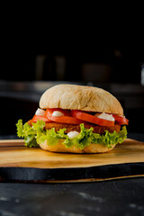 Classic hamburger with pork cutlet, tomato, salad leaves, white sauce with french fries on the wooden plate on the dark background   
