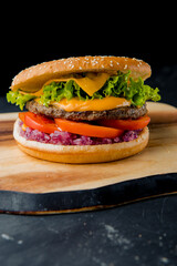 hamburger with beef cutlet, tomato, salad leaves, cedar cheese, red marinated onion with french fries on the wooden plate on the dark background   