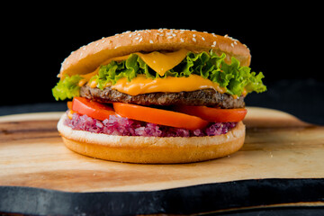hamburger with beef cutlet, tomato, salad leaves, cedar cheese, red marinated onion with french fries on the wooden plate on the dark background   