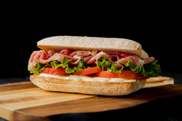 healthy delicious sandwich with salad leaves, prosciutto crudo, tomato, white sauce on the wooden board, dark background  