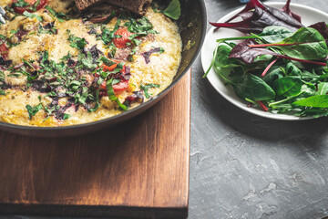 Cooked omelette with sausage, cheese, tomato and herbs in a pan, on wooden board