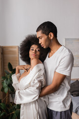 african american man embracing seductive girlfriend in white satin robe in bedroom
