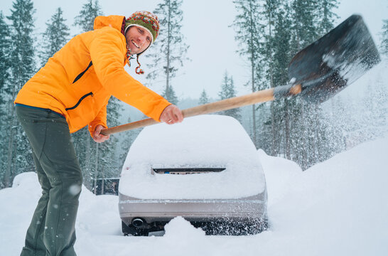 Winter Morning Routine. Smiling Man With A Shovel Removing Snow From The Path And Cleaning Auto. Car Covered With Snow As A Huge Snowdrift On The Countryside Forest Home Driveway.